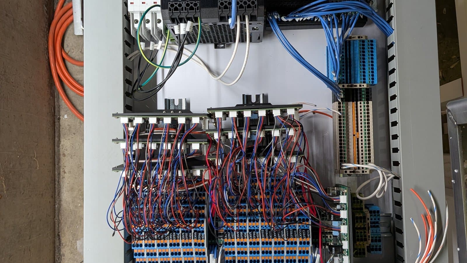 Open industrial control panel showing dressed red and blue wiring, labeled terminal blocks and a PLC