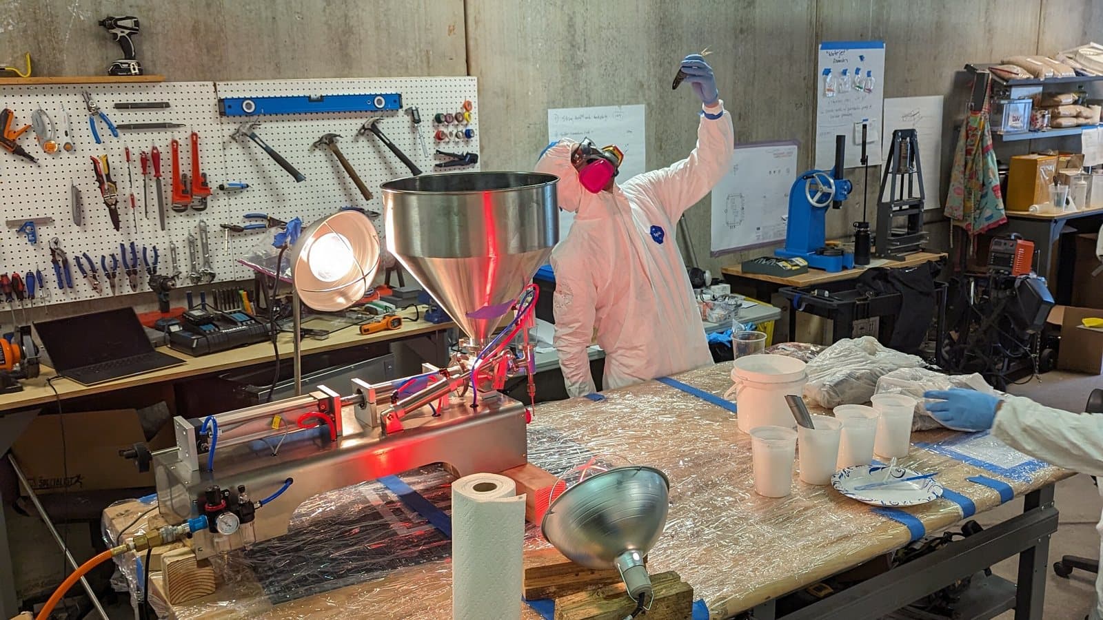 Engineer in a protective suit testing a benchtop process rig on a shop bench, tool wall behind