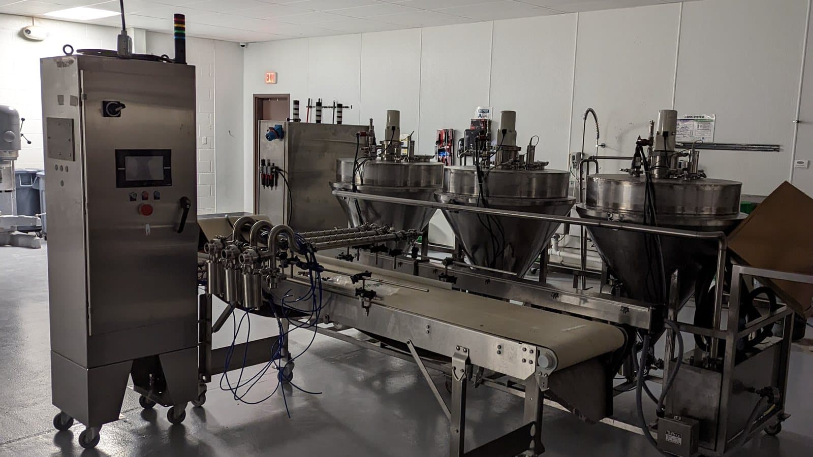 A row of identical hopper depositor units feeding a single conveyor, with the control cabinet at left